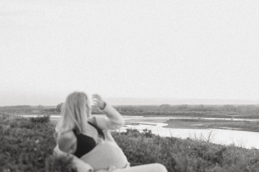 Black and white photo of a person lounging on a hillside overlooking a scenic waterway.