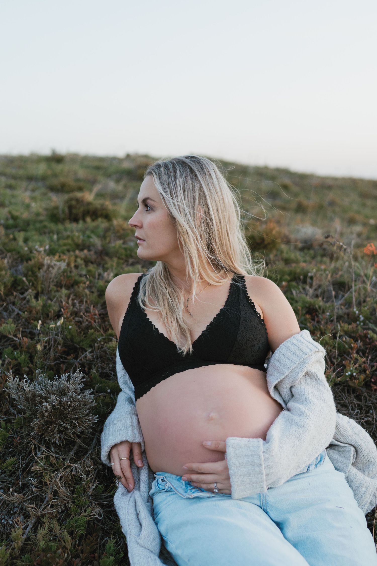 Maternity photo in nature showing pregnant belly against heather-covered hillside at dusk.