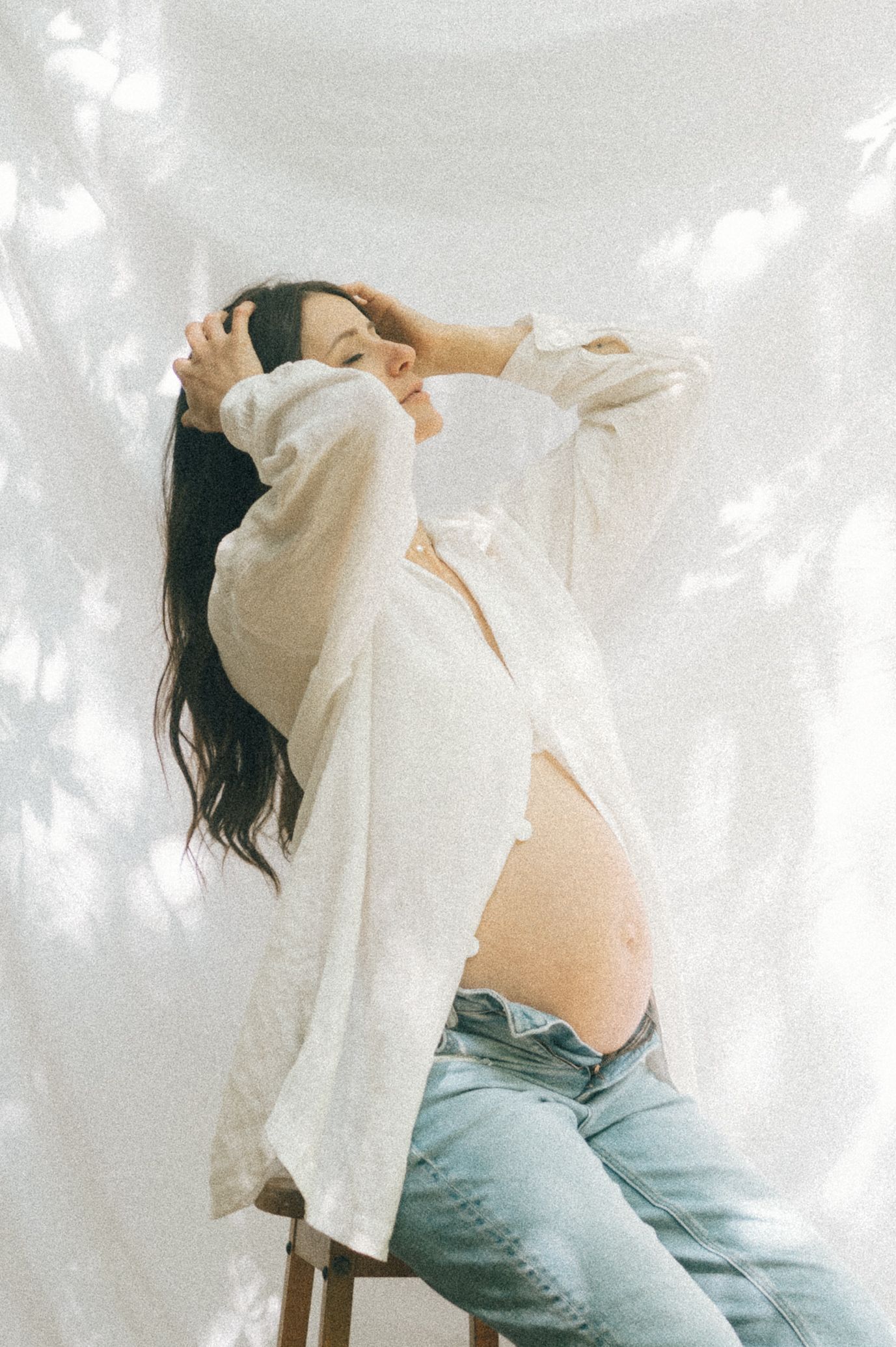 Artistic maternity photo with white button-down shirt and denim in natural lighting.