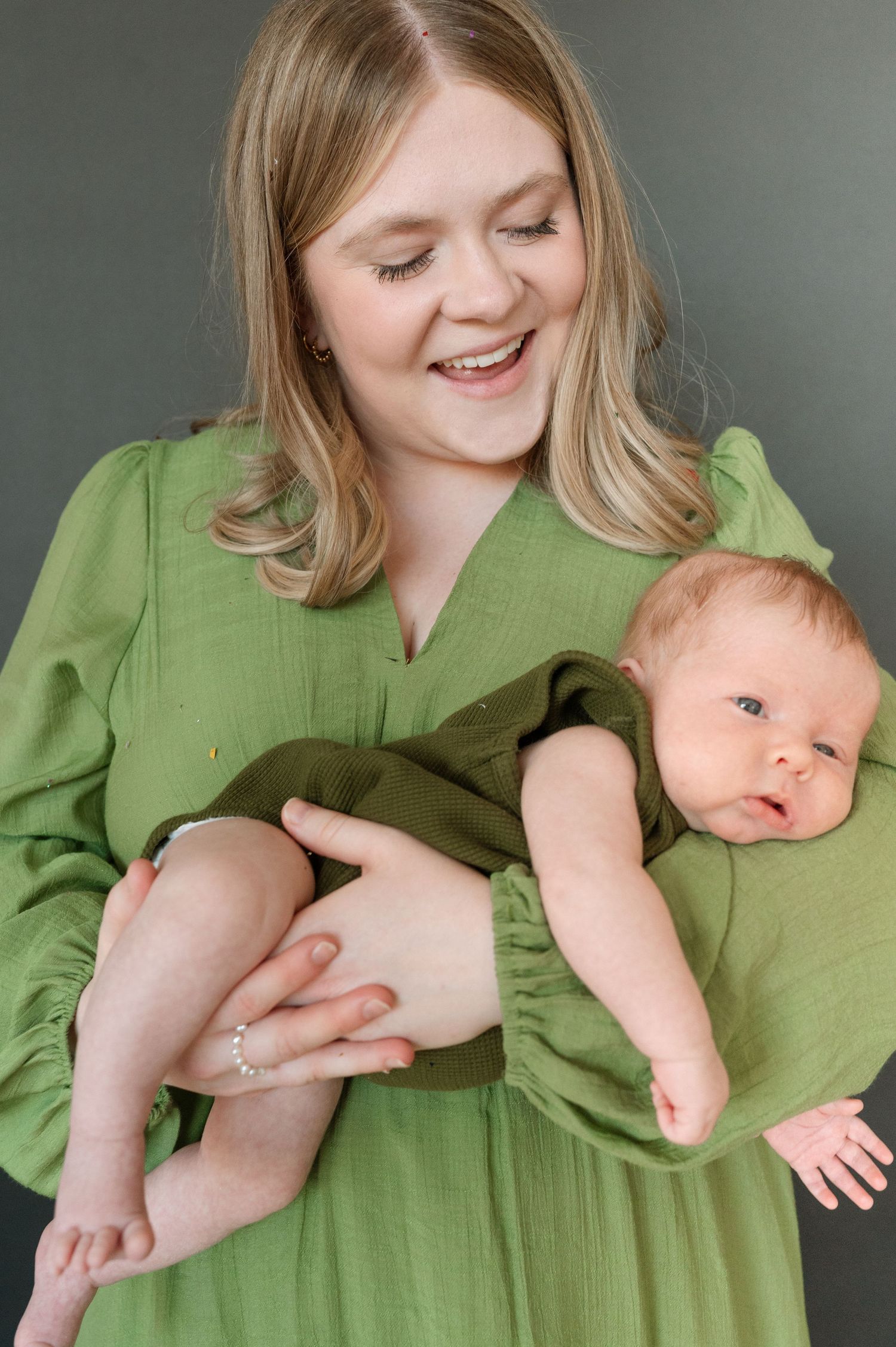 A tender moment between parent and baby as they share a joyful interaction while wearing matching green outfits.