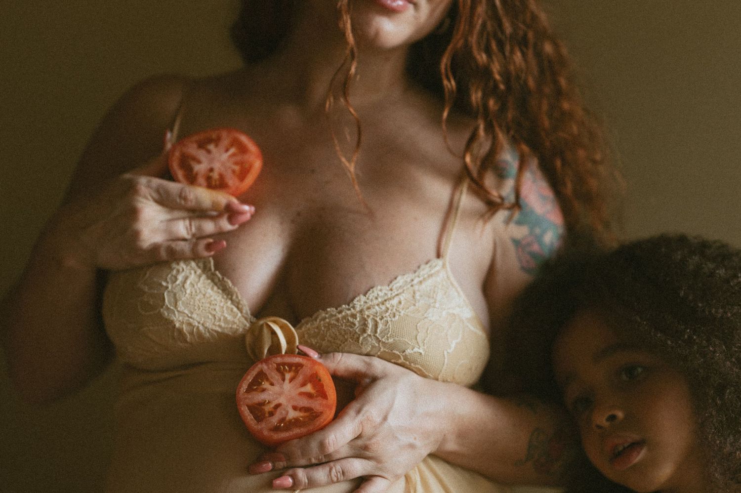 Person in lace lingerie holding sliced tomatoes in a moody indoor setting.