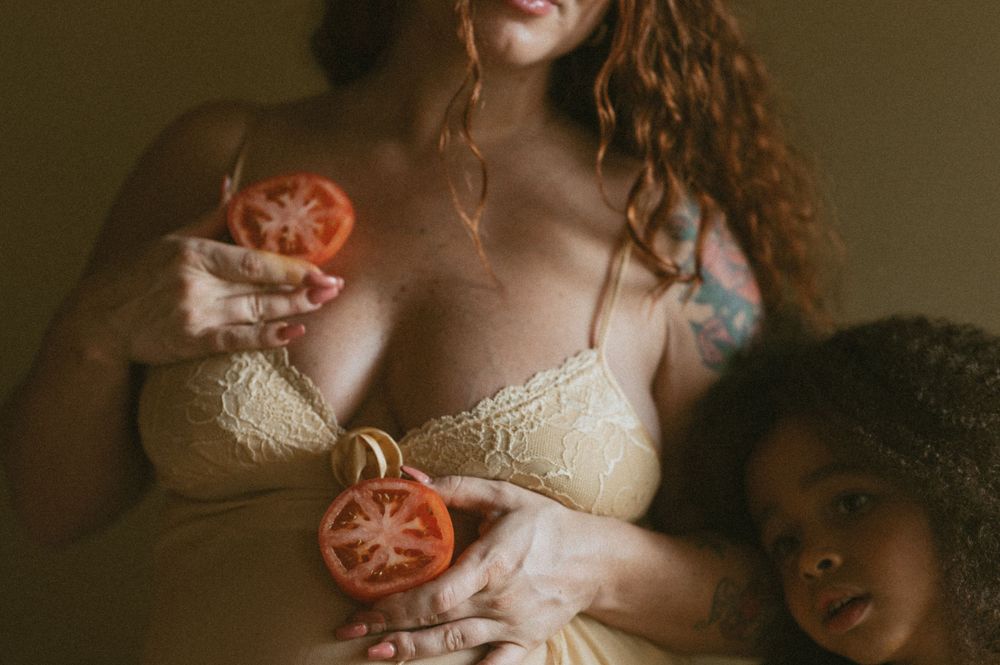 Person in lace lingerie holding sliced tomatoes in a moody indoor setting.