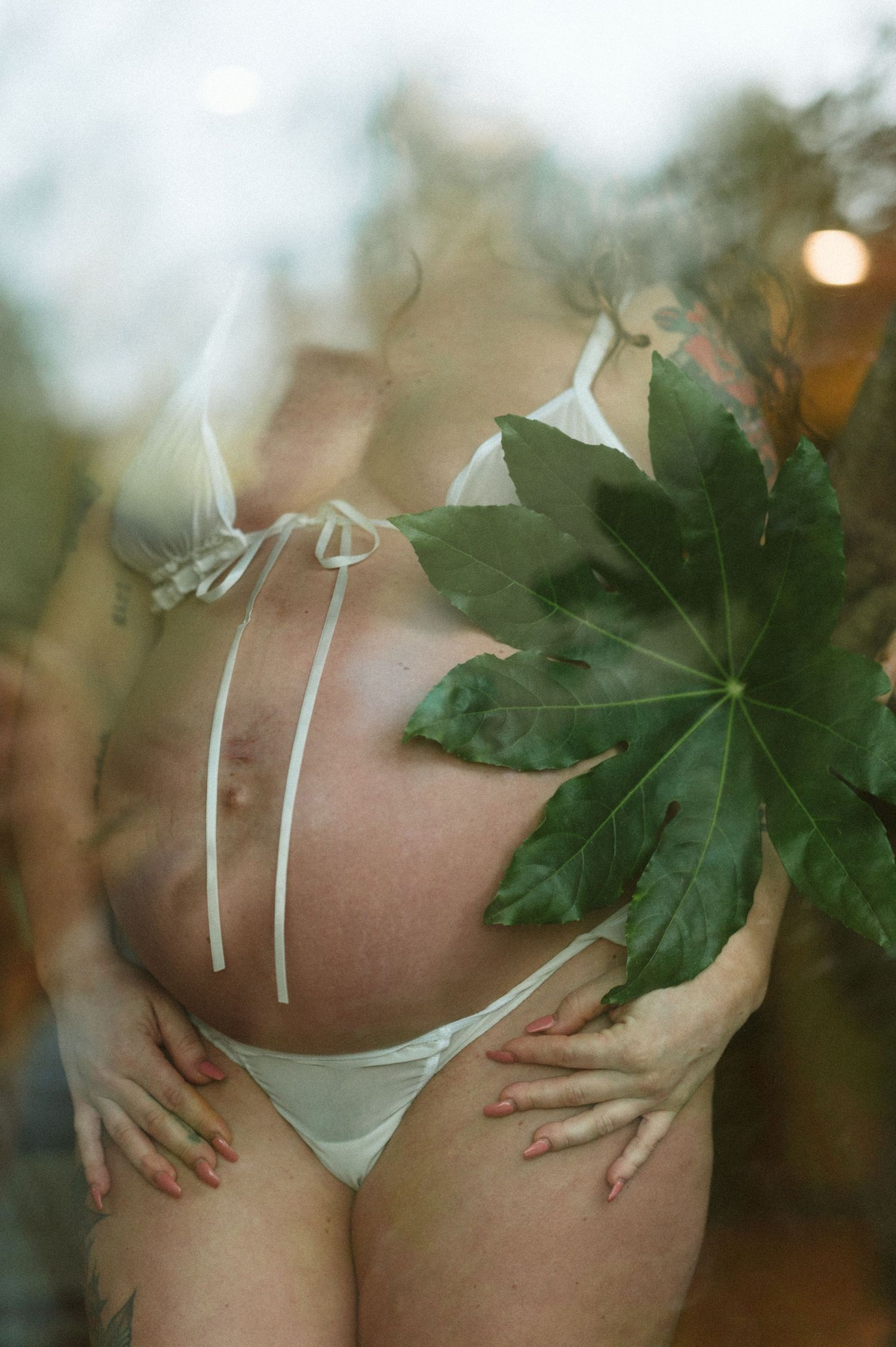 Artistic maternity photo with maple leaf and white lingerie in soft focus.