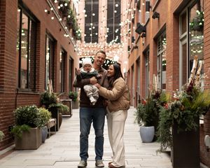 People walk through a brick-lined shopping arcade decorated with hanging string lights and planters.