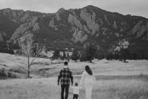 Black and white photo of couple walking through field with mountain backdrop.