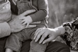 A black and white close-up of hands tenderly holding each other.