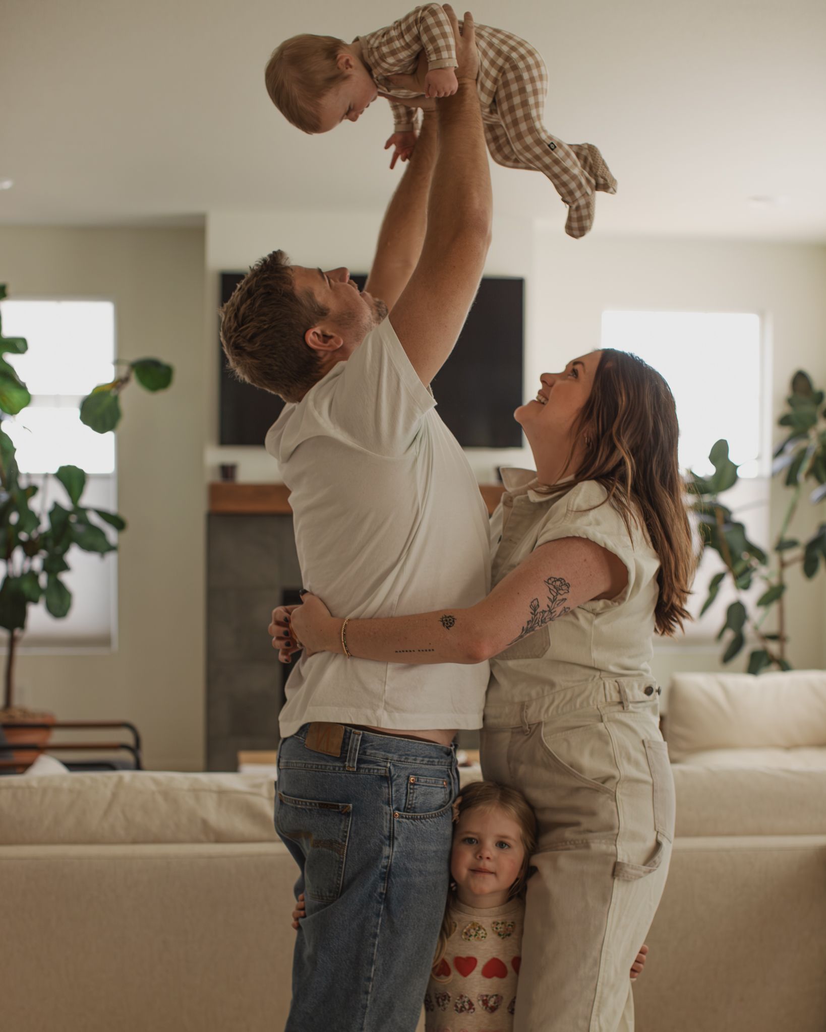 A family shares playful moments together in their bright living room with houseplants in the background.