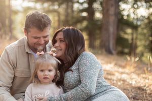 Intimate family portrait captured in warm evening light among pine trees.