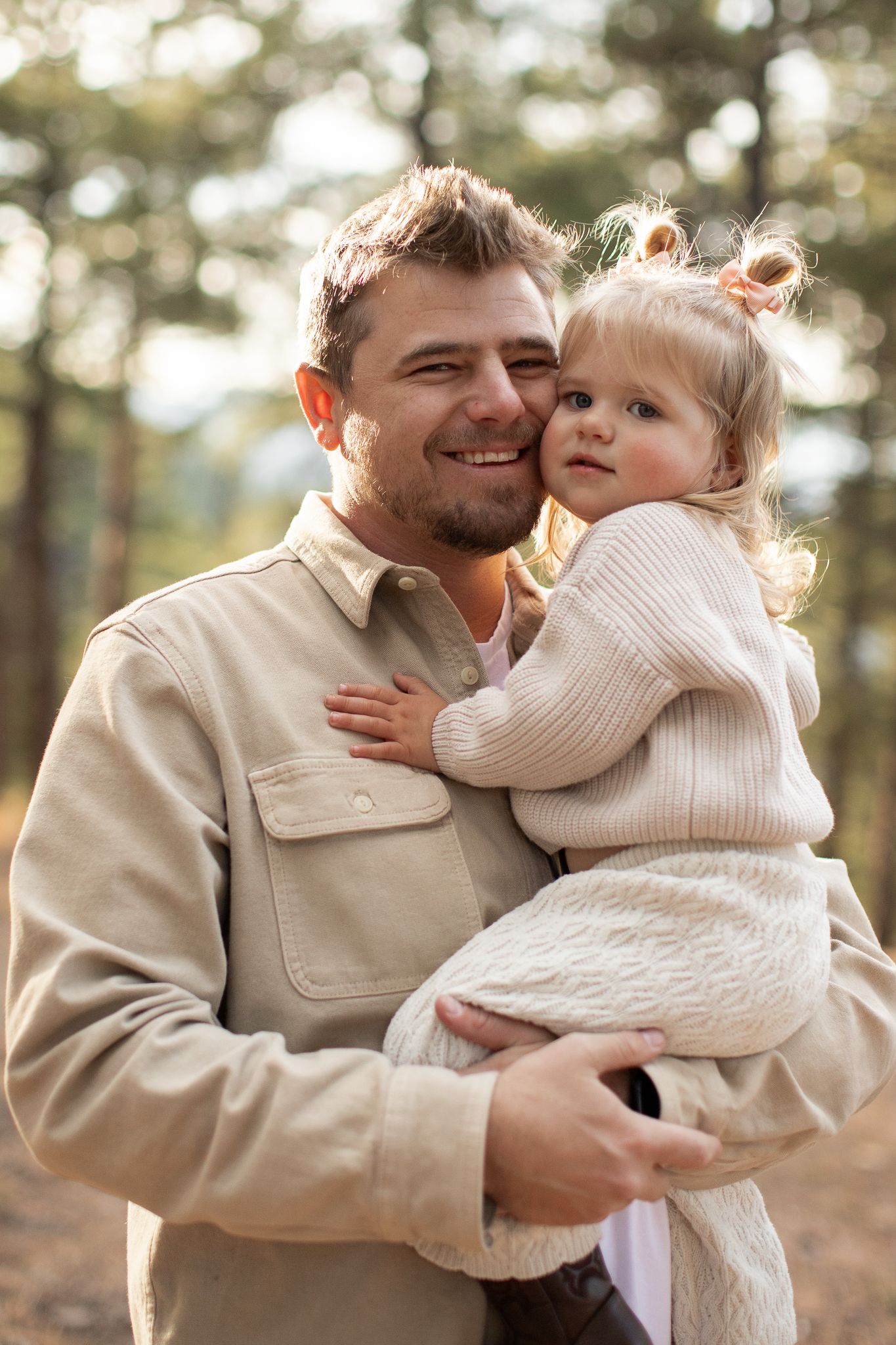 Candid outdoor portrait of parent and toddler wearing cream colored sweaters in a forest setting.