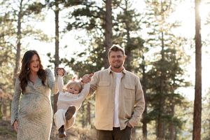 Family enjoying a playful moment together outdoors with pine trees in background.