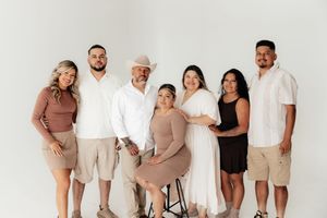 A joyful family of seven poses together in a bright white studio, wearing neutral and earth-toned outfits.