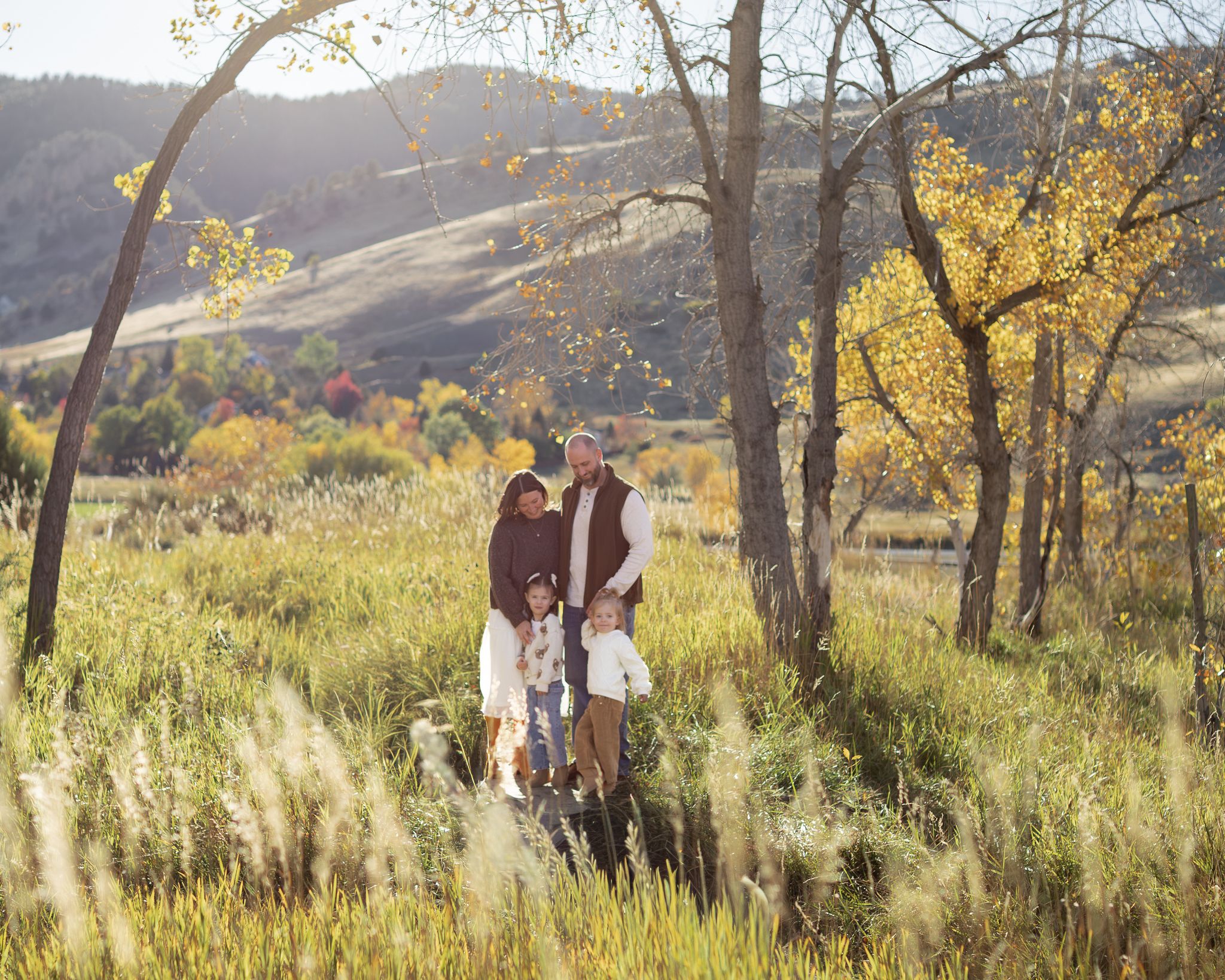 Family walking together through tall golden grass in a scenic mountain landscape at sunset.