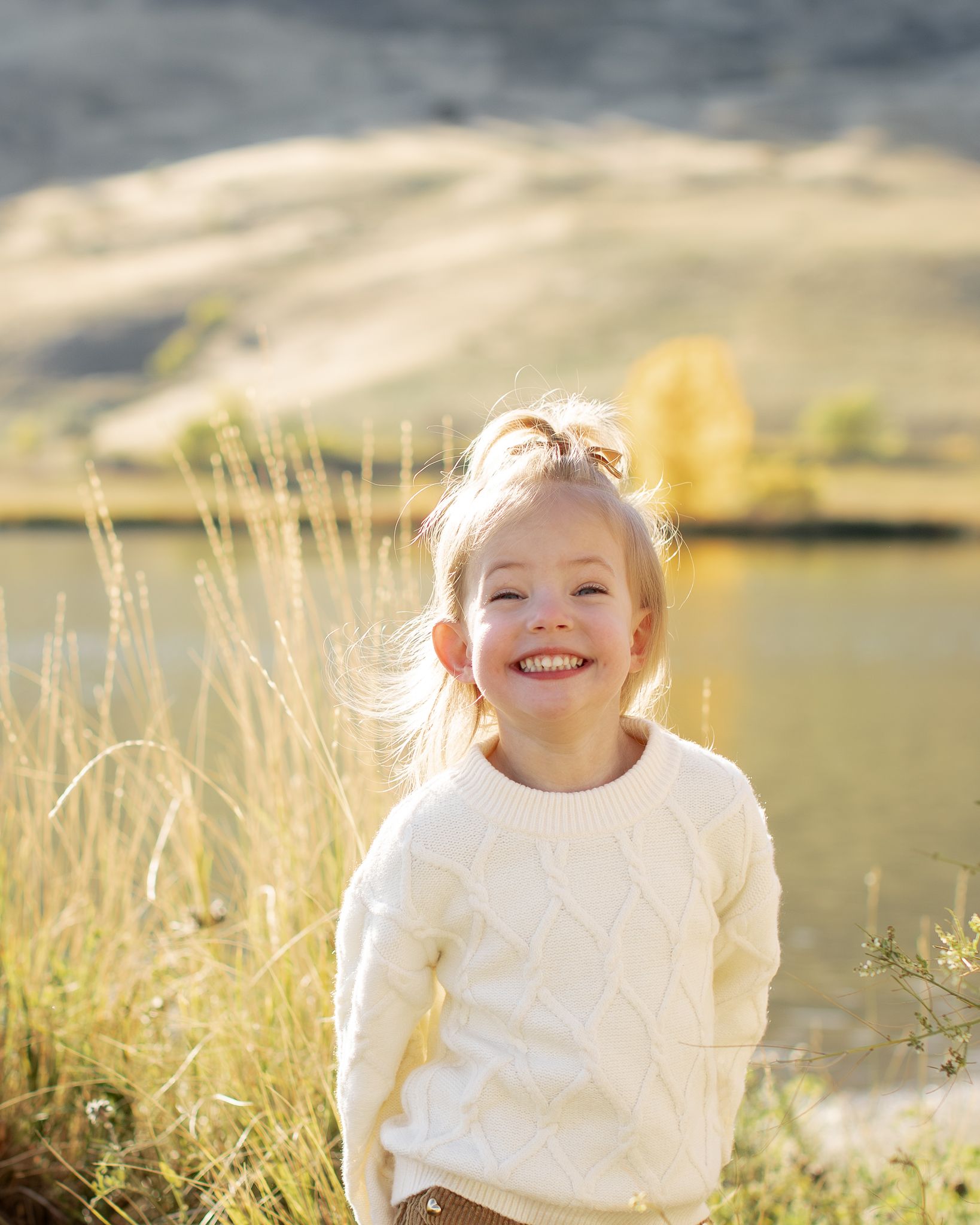 Child playing in tall grass field with mountains in background during golden hour.
