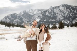 A family enjoying a winter day together in the snow with mountains as their backdrop.