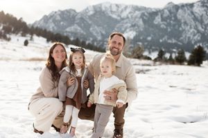 Happy family posing together in snowy mountain landscape wearing neutral colors.