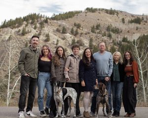 A group of people standing together outdoors with mountains and trees in the background on a cloudy day.