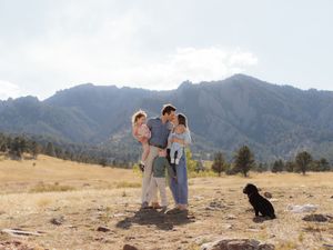 Family with two young children and black dog posing in rocky mountain meadow with Flatirons in background.