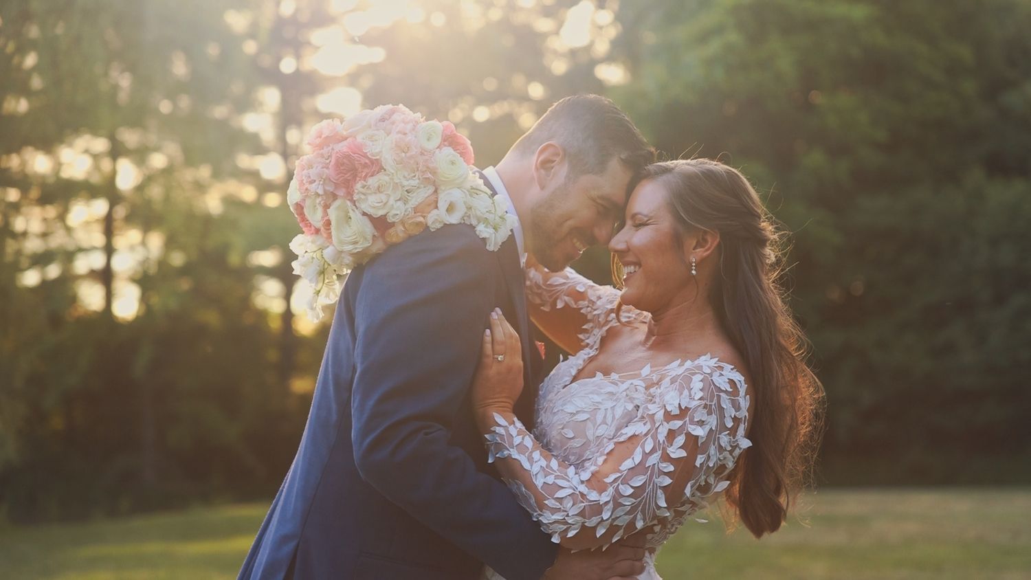A couple shares a romantic moment in nature at sunset, with soft lighting illuminating their embrace.