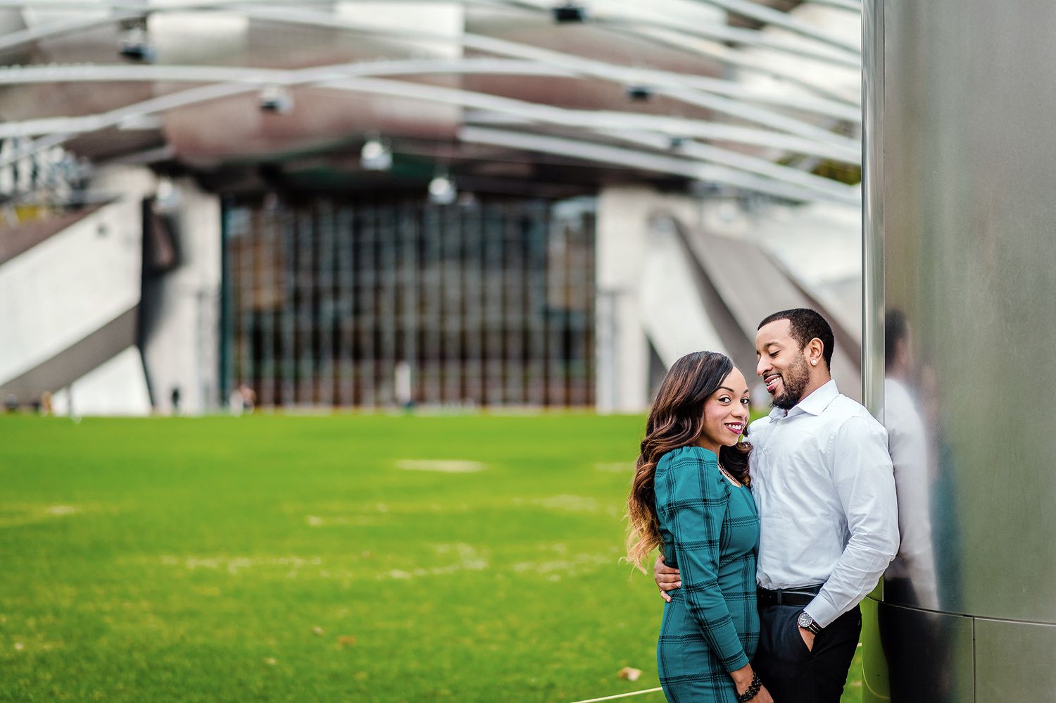 Couple sharing romantic moments together in an outdoor setting with modern architecture in the background.