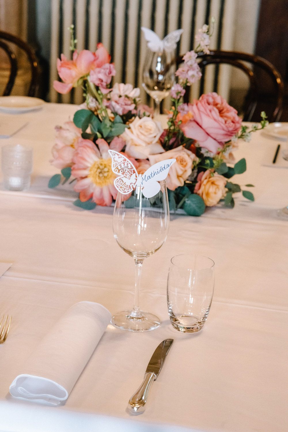 Intimate wedding dinner table set with coral flowers, tall pink taper candles, and white linens