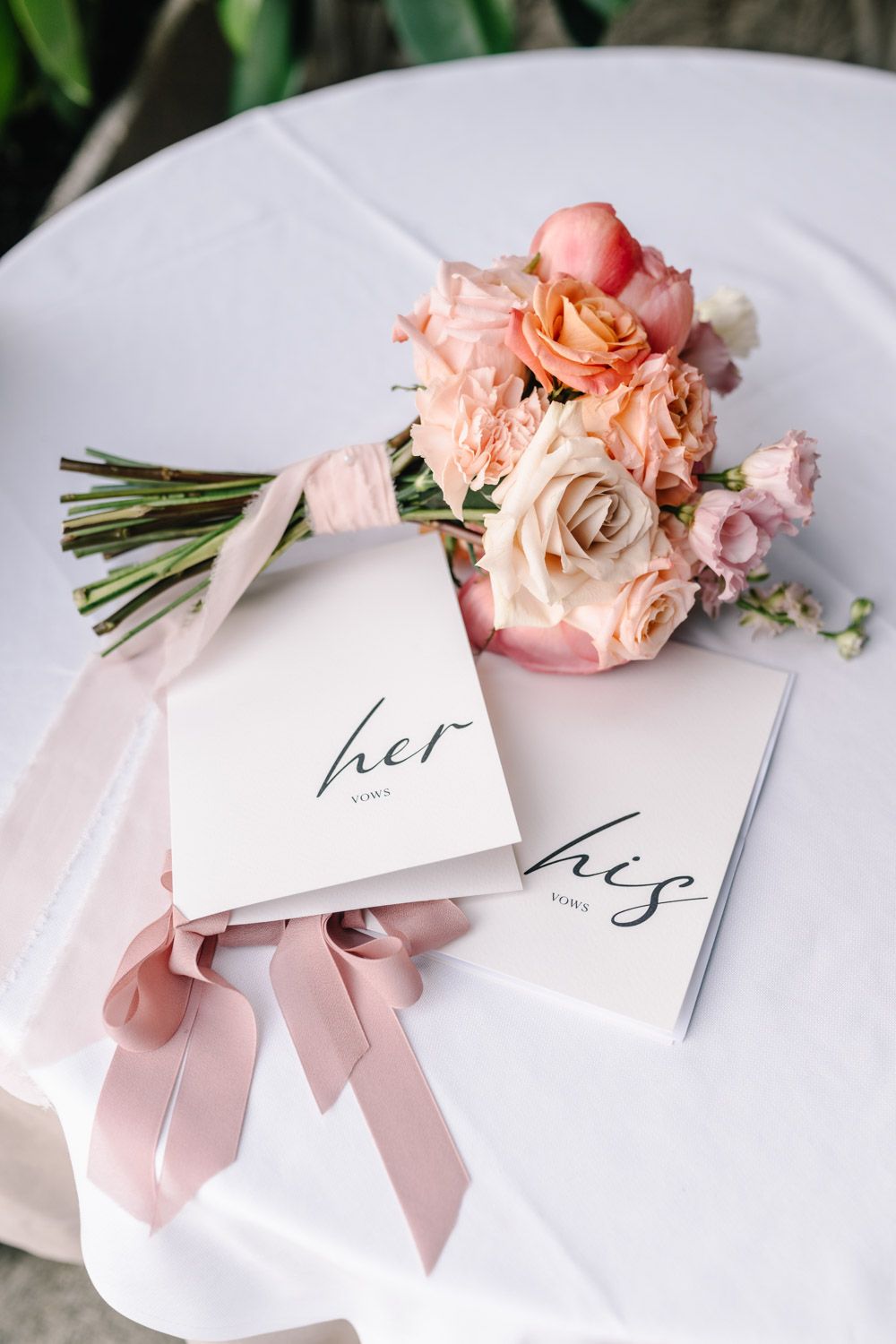 Close-up of vow covers and bridal bouquet with coral, pink, and peach roses for a spring elopement