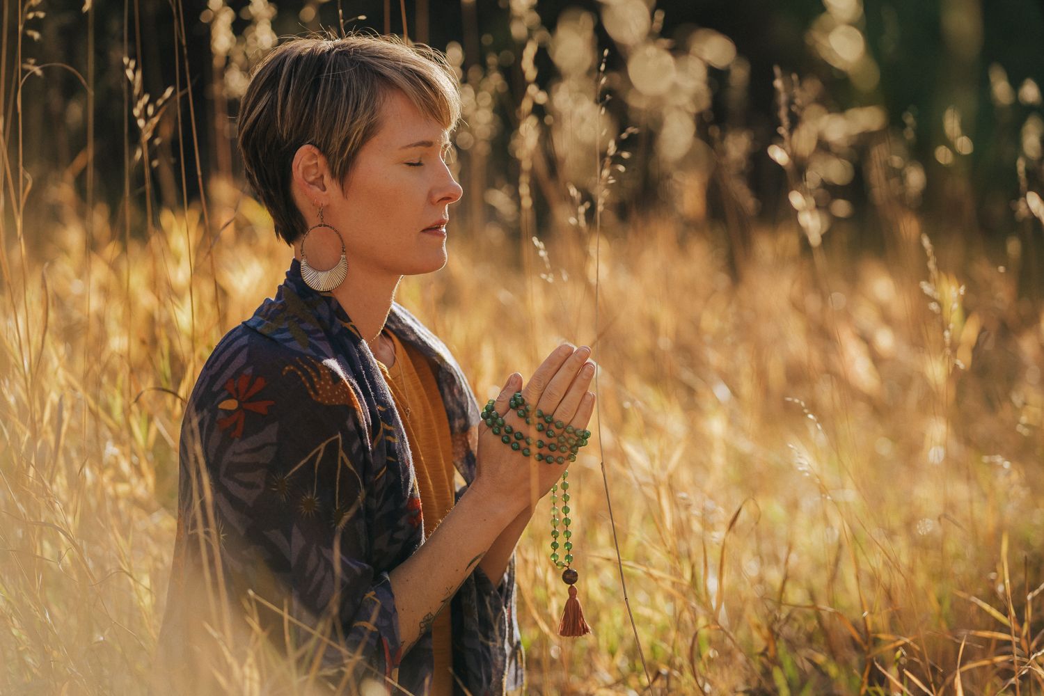 Young child in denim jacket walking through a golden field of tall grass at sunset with warm backlighting.