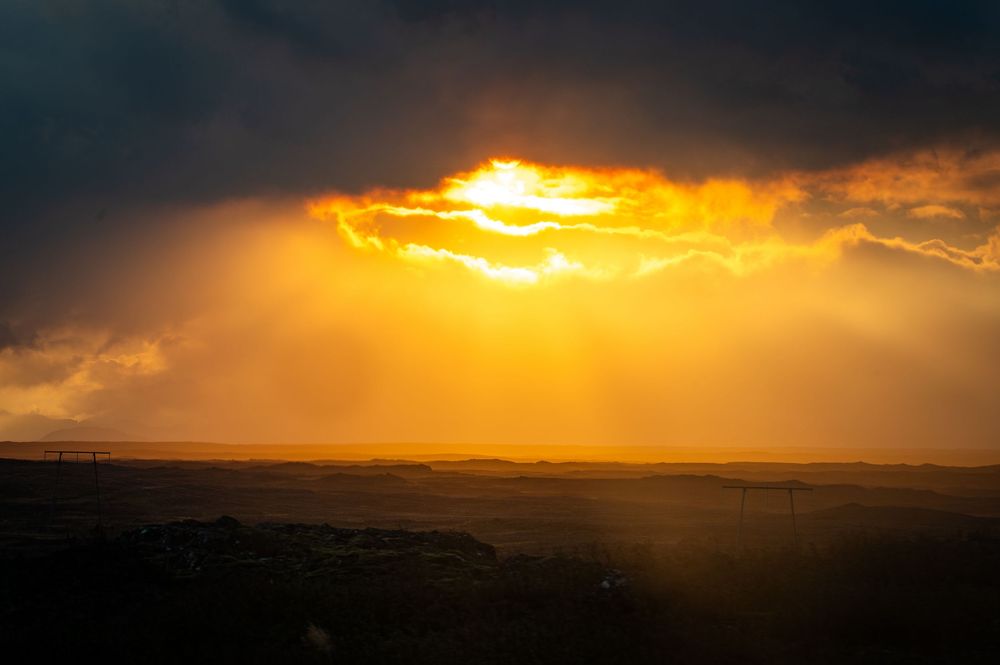 Dramatic orange sunset breaking through dark storm clouds over a silhouetted landscape.