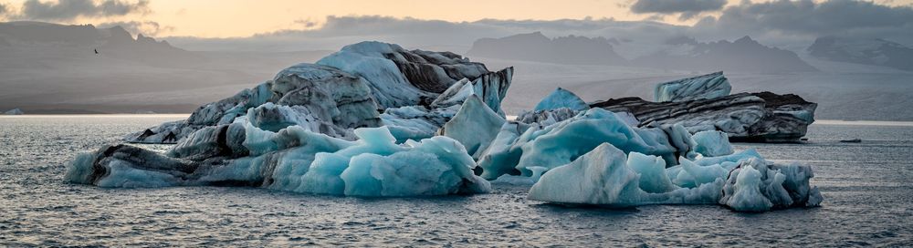 Dramatic glacier ice formations on a black sand beach with stormy clouds at sunset.