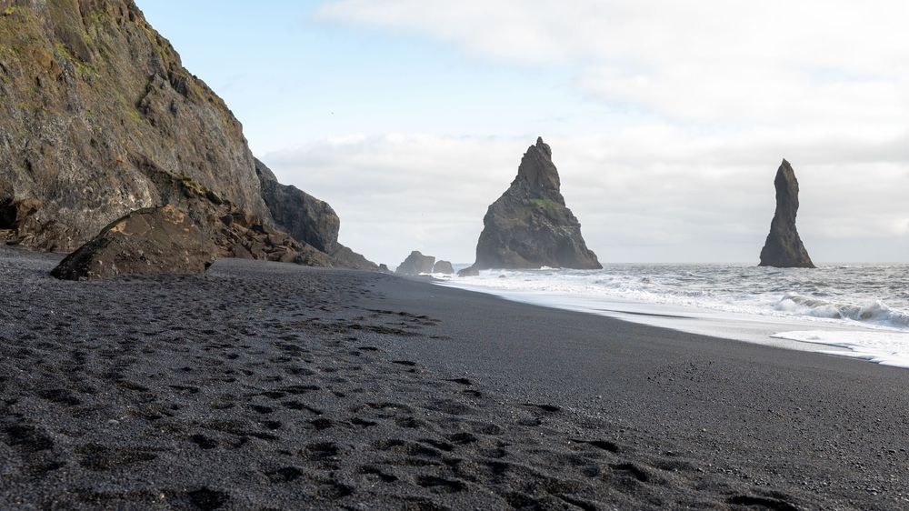 Dramatic black sand beach in Iceland with towering sea stacks and cliffs along the rugged coastline.