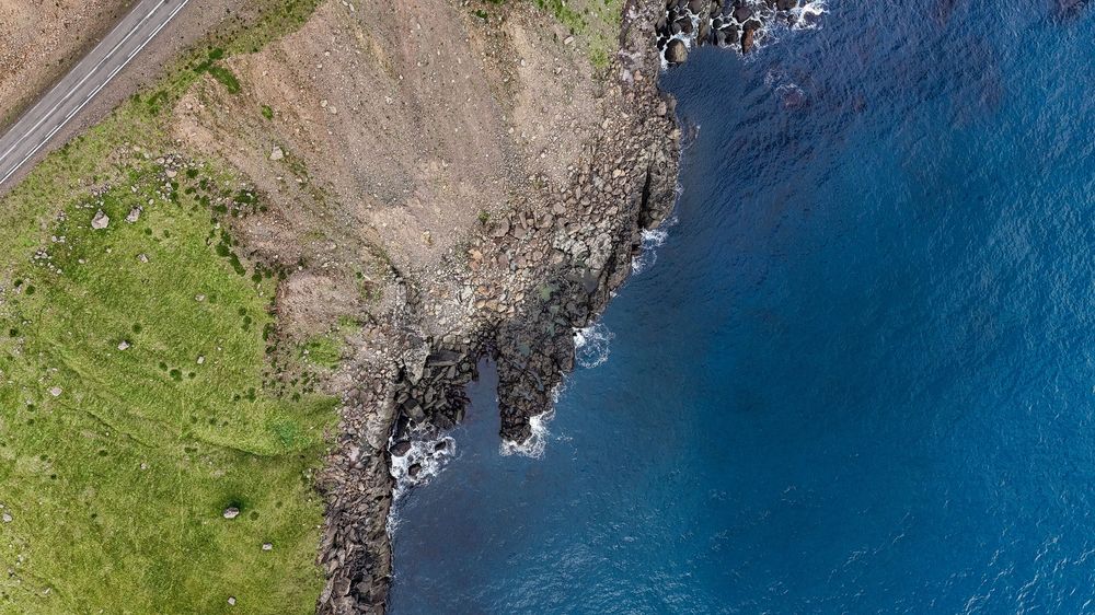 Aerial view of rugged coastal cliffs meeting deep blue ocean waters in Iceland.