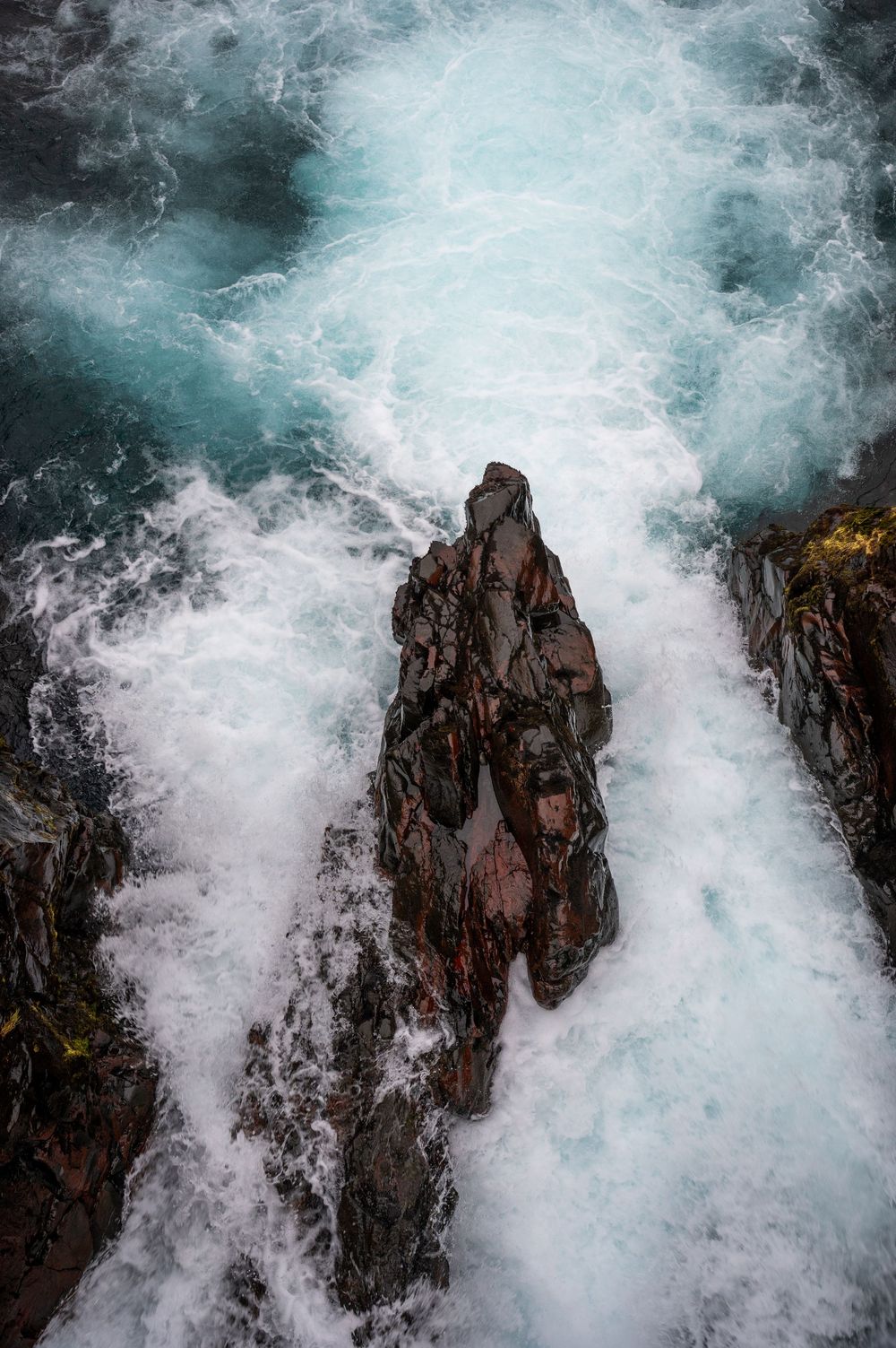 Dramatic ocean waves crashing against dark rocky cliffs creating white water spray.