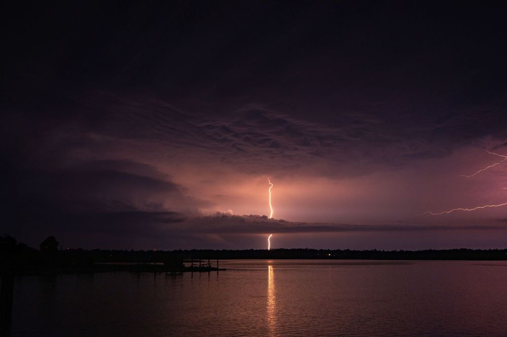 Lightning bolt strikes over a dark lake at night creating a dramatic reflection on the water's surface.