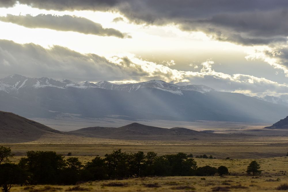 Dramatic panoramic view of sunlight breaking through storm clouds over a mountainous desert landscape at sunset.