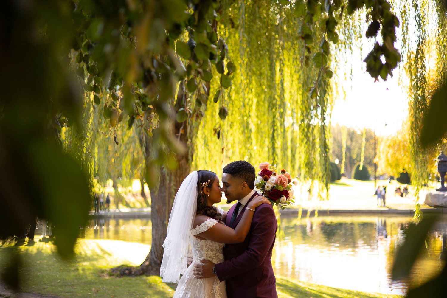 A married couple shares a romantic moment under a weeping willow tree near a tranquil lake during golden hour in Boston's Public Gardens.