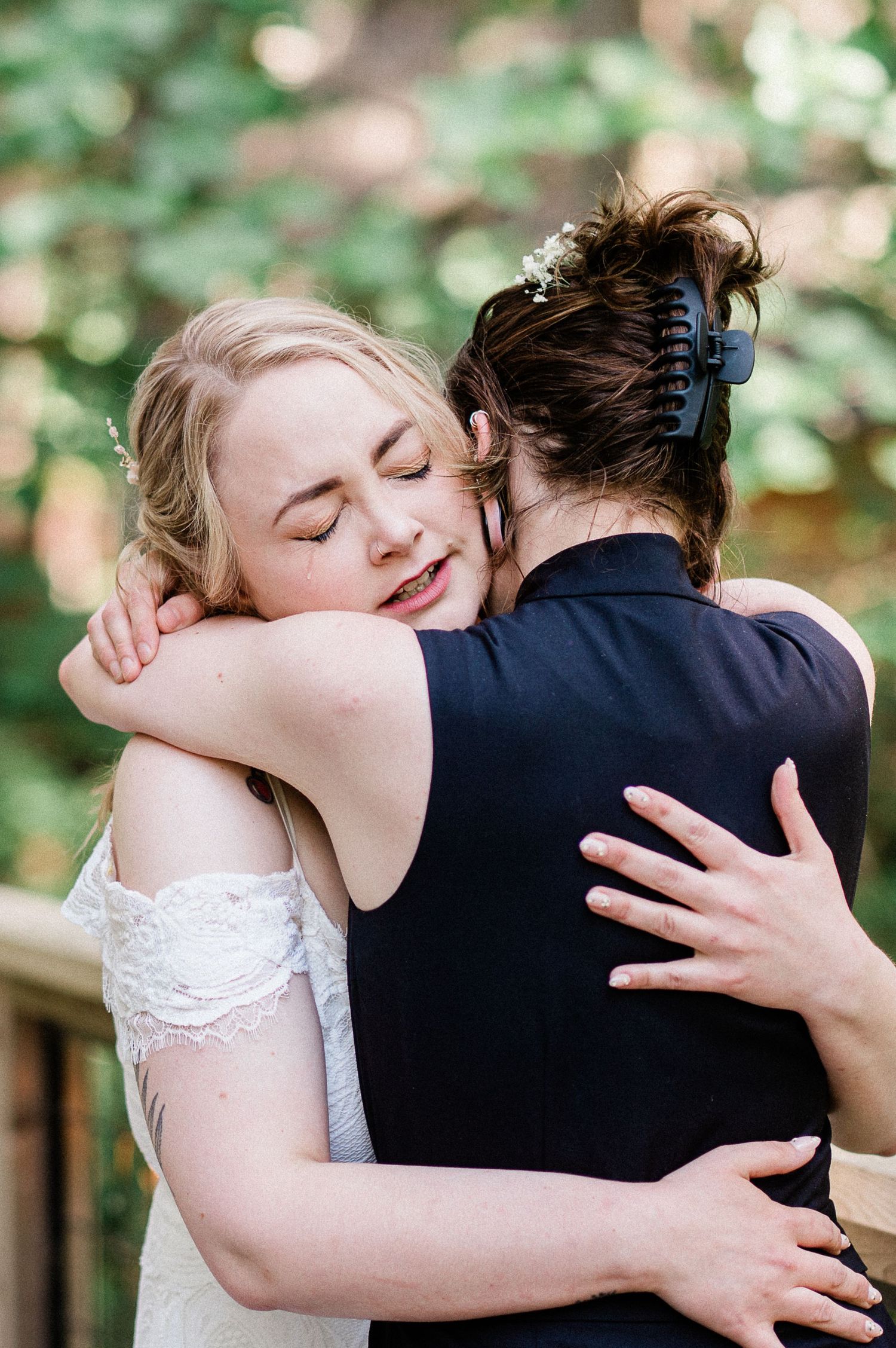 Close up of two brides hug while tears roll down their face.