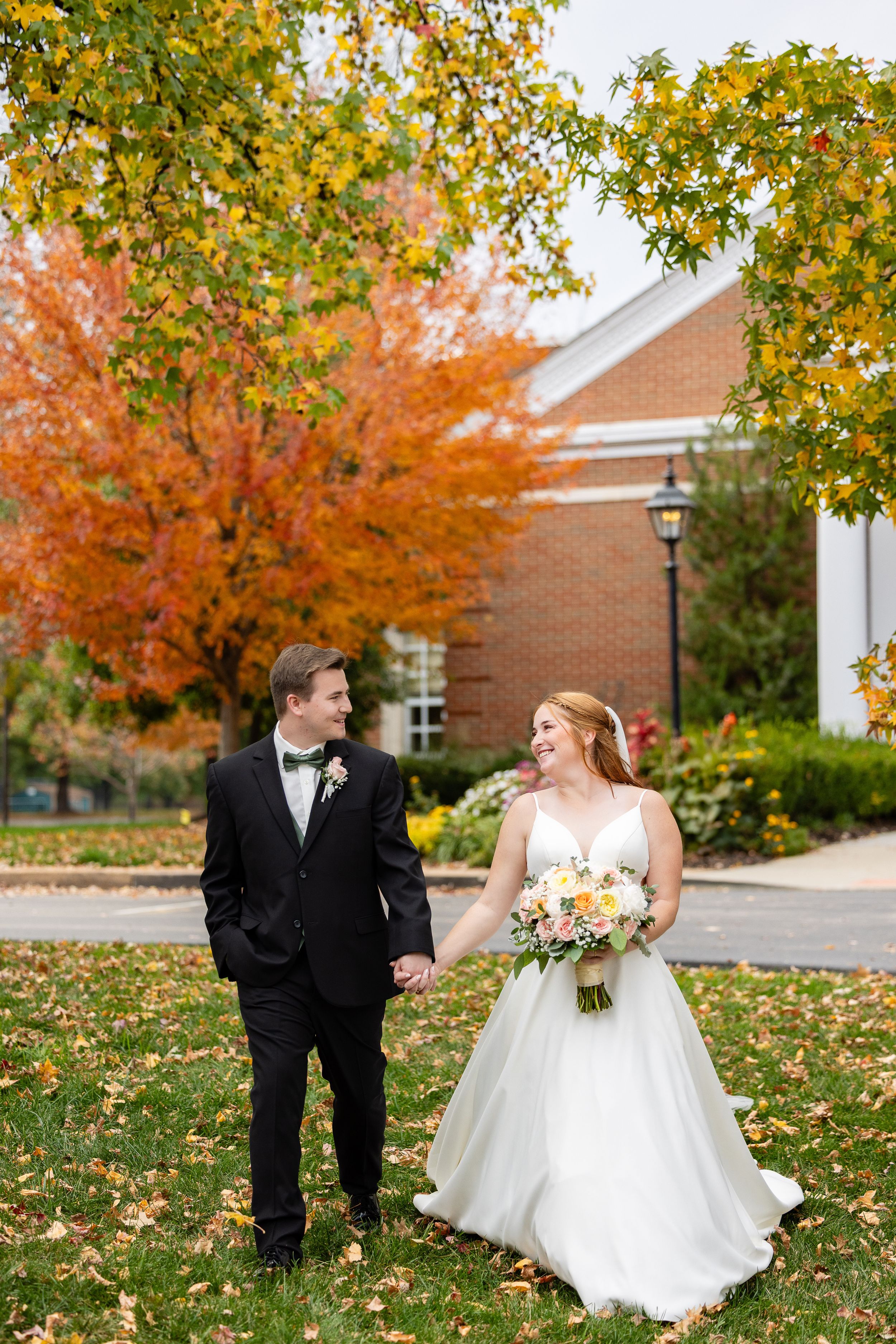 A large wedding party posing together outdoors in front of a building.