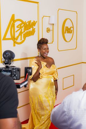 Woman in yellow gown laughing on red carpet at 40th Stellar Awards with P&G branding backdrop.