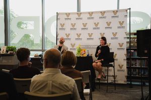 Two speakers on stage at a Vanderbilt University panel discussion event in a modern library setting.