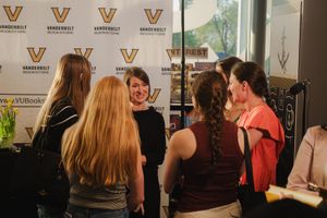 Students gather around a smiling author at a Vanderbilt University book signing event near VUBooks display.