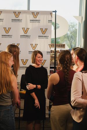 A woman in black dress smiles while conversing with a group at a Vanderbilt Bookstore event.