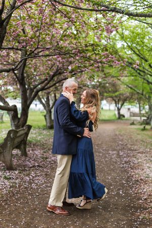 A romantic couple embraces under blooming cherry blossom trees on a spring path.