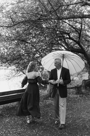 A couple shares a romantic moment under a white umbrella in a park, captured in black and white photography.