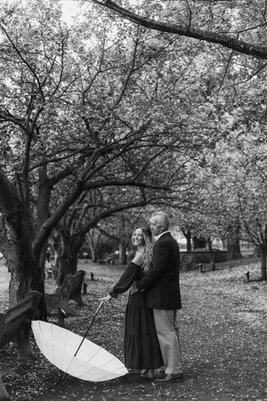 Couple with white umbrella posing among cherry blossom trees in black and white.