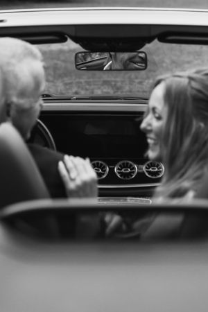 Black and white view through car interior showing dashboard gauges and rearview mirror reflections.
