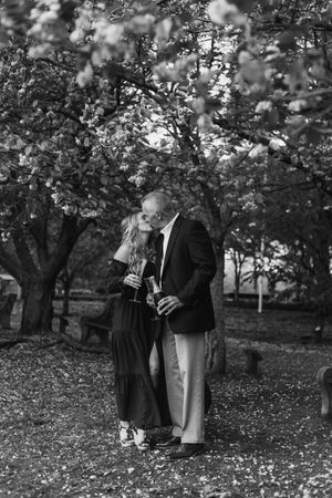 Two figures stand together in an orchard with fallen leaves on the ground in black and white vintage photography.