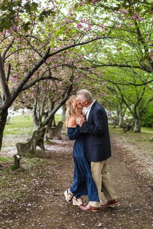 Romantic couple embraces under blooming cherry trees in a spring garden setting.