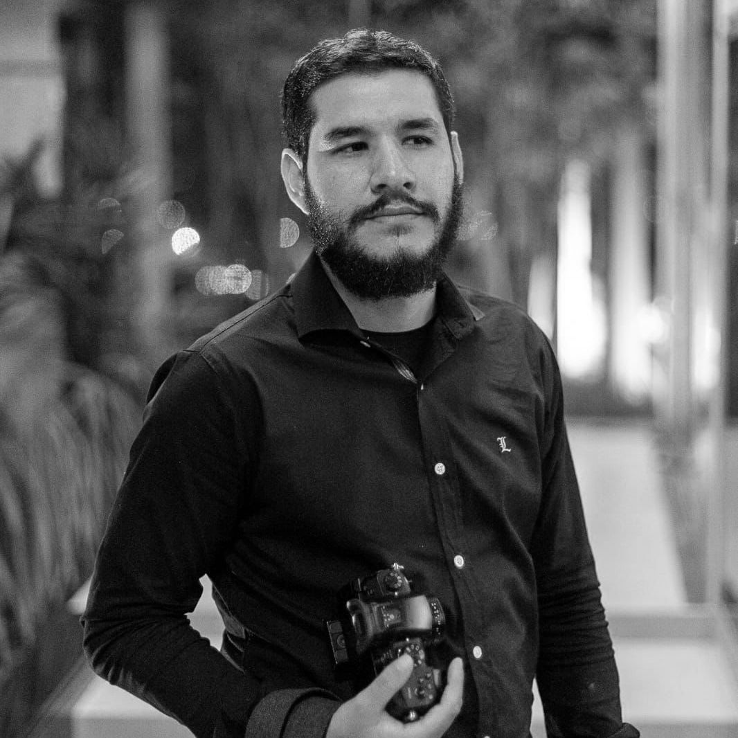 Black and white portrait of photographer with beard holding camera outdoors.