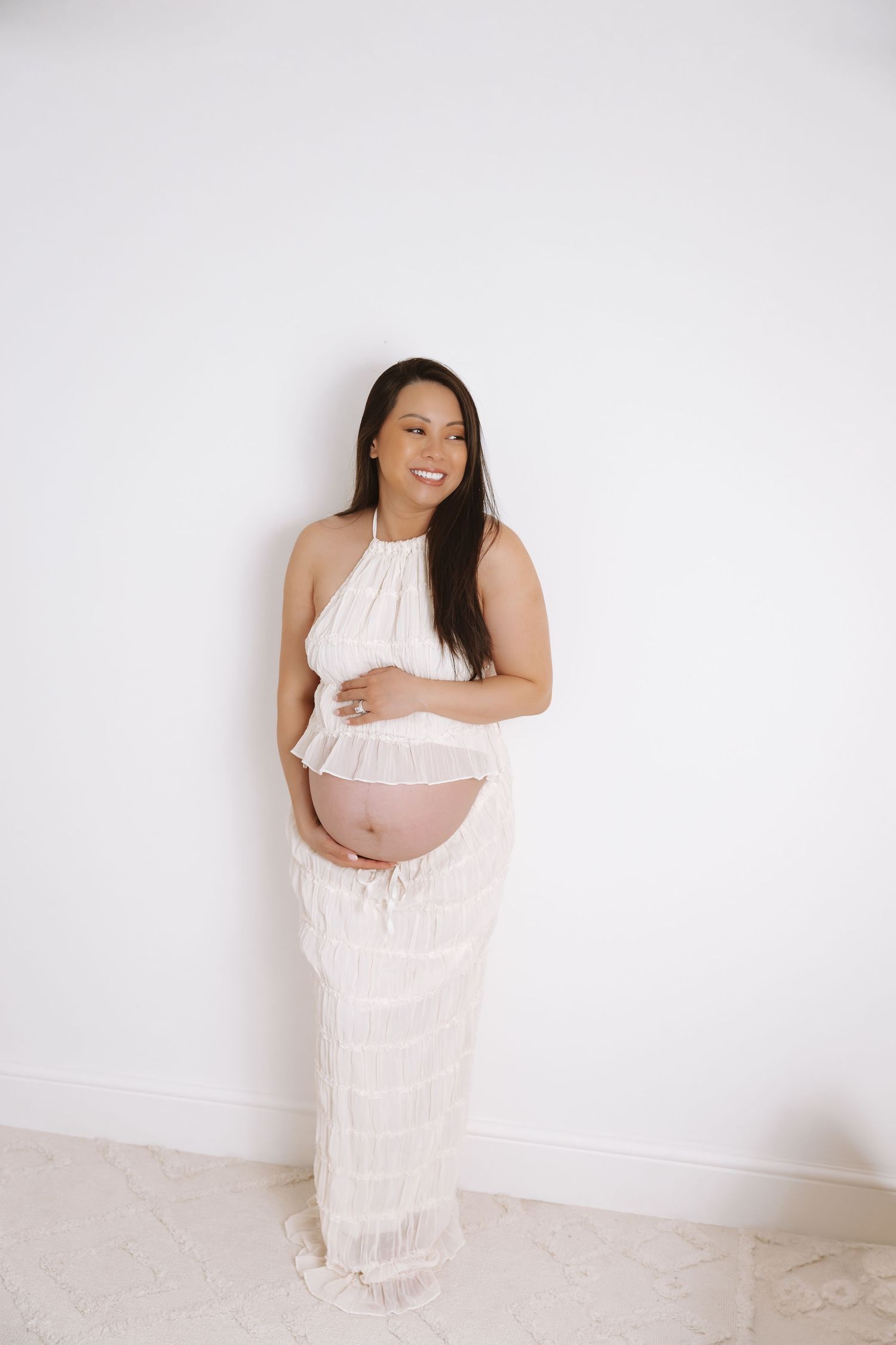 A maternity photoshoot featuring a person wearing a white flowing dress against a white backdrop.