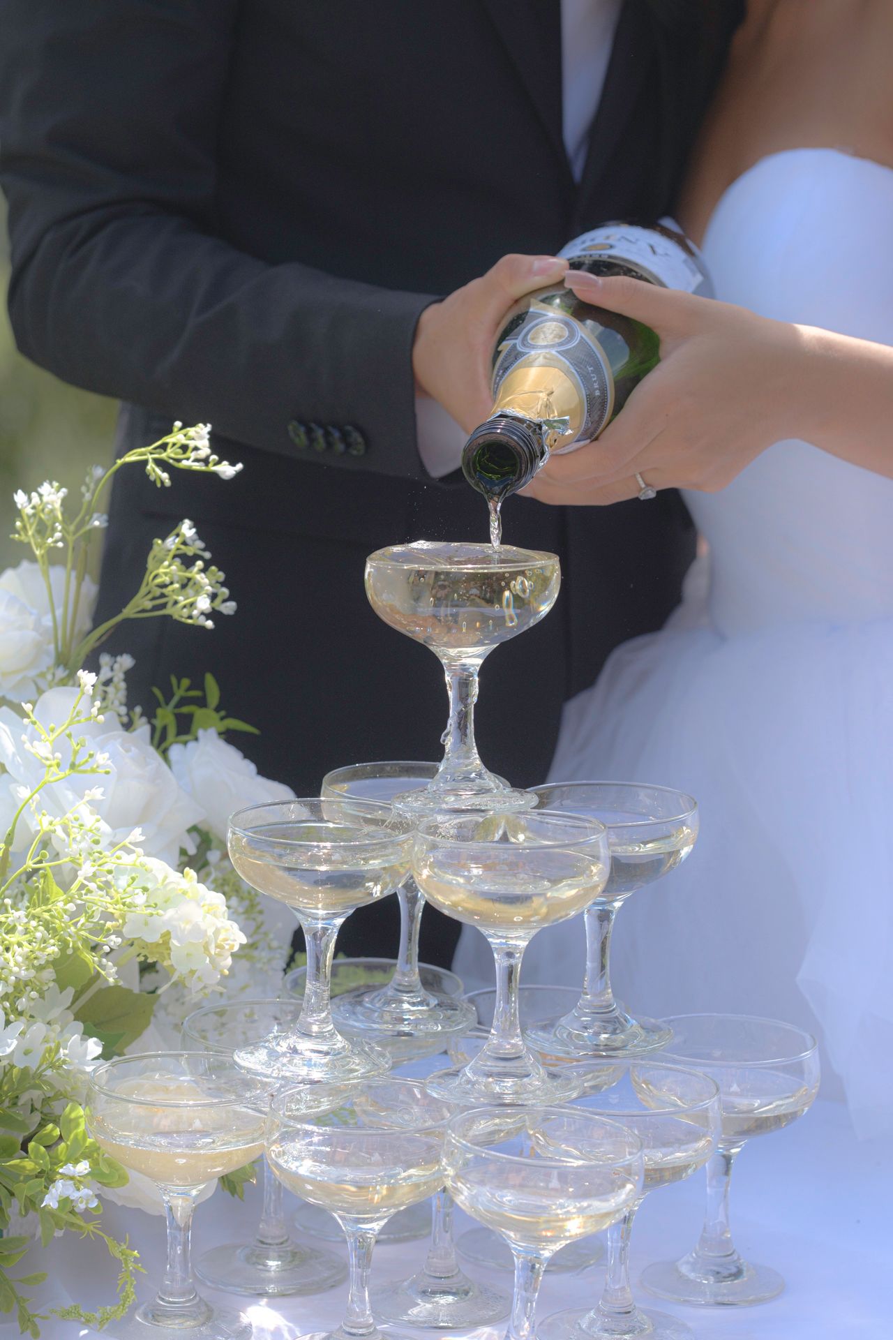 Champagne being poured into a wedding champagne tower surrounded by white floral arrangements during a Hawaii wedding celebration.