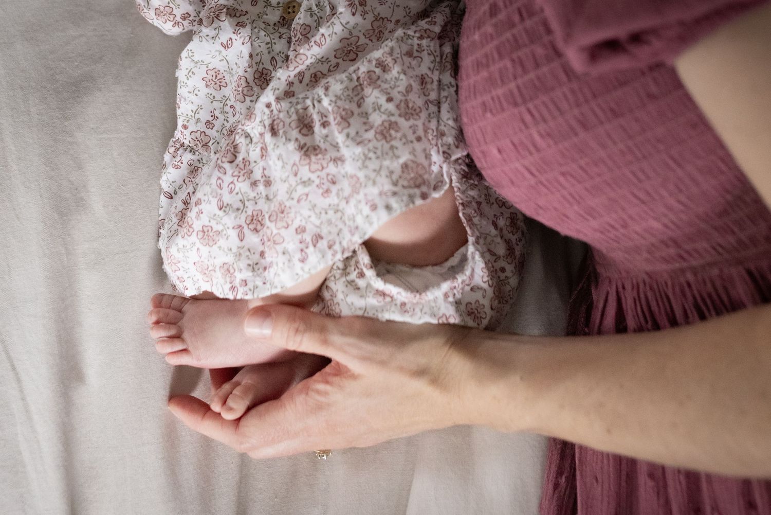 Close-up of a parent cradling a newborn baby's tiny feet in their hands, with soft pink fabric in the background.